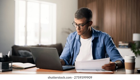 Documents, laptop and remote work with man in home study for planning, research or review. Computer, paperwork and report with freelance employee at desk in apartment for small business startup