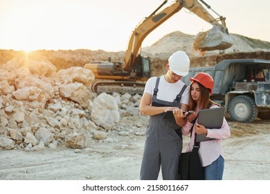 With documents. Two workers is on the borrow pit at daytime together.