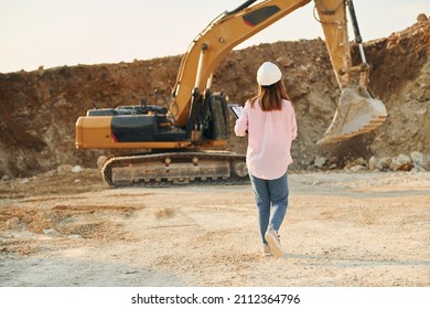 With documents. Young woman with documents in hard hat is standing on the borrow pit.