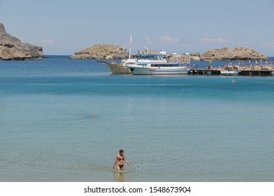 Dodecanese, Greece - May 19, 2010: Scene With Swimmer Coming Out Of The Water At Lindos Beach And Pleasure Boats Trapped In A Jetty In The Background Of The Image