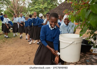 Dodoma, Tanzania. 08-18-2019. An african smiling girl is washing hands after having lunch at school while other students are waiting in line.