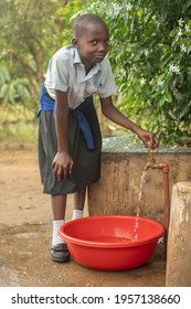 Dodoma, Tanzania. 08-18-2019. A beautiful black girl is looking at the camera while filling a bucket of water to clean the dishes after lunch in Tanzania.