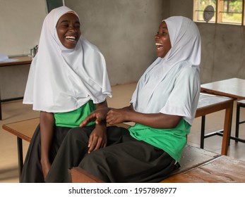 Dodoma, Tanzania. 08-18-2019. Portrait of two female muslim black adolescents having great fun and laughing inside their classroom at a rural school in Tanzania.