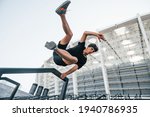 Does parkour. Young man in sportive clothes have workout outdoors at daytime.