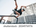 Does parkour. Young man in sportive clothes have workout outdoors at daytime.