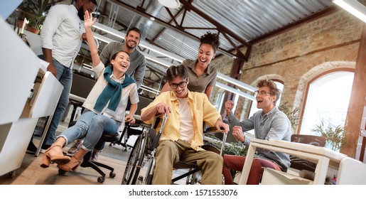 Does Work Make You Happy. Young Positive Asian Man In Wheelchair Having Fun With His Colleagues At Modern Office