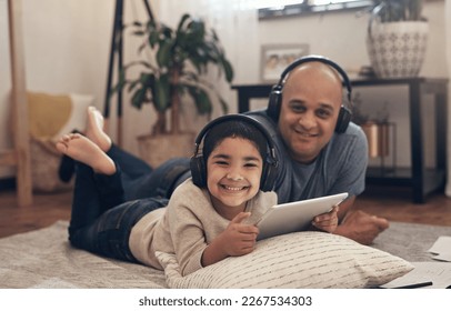 It doesnt feel like schoolwork when its so much fun. Shot of an adorable little boy using a digital tablet and headphones with his father at home.