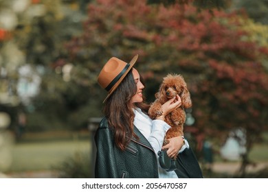 Dog. A Beautiful Young Dark-haired Woman Walks In The Park And Hugs Her Poodle. Autumn Mood. Fall.