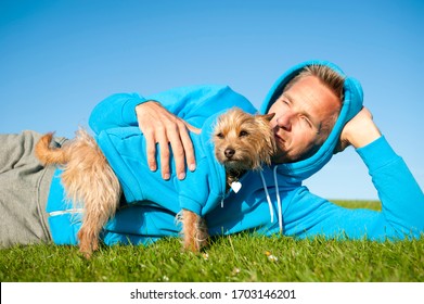 Dog And Best Friend Owner In Matching Blue Hooded Sweatshirts Bonding Outdoors On Sunny Green Field