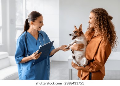 Dog held by its female owner during vet consultation, with friendly veterinarian taking notes, illustrating positive veterinary visit and pet care interaction - Powered by Shutterstock