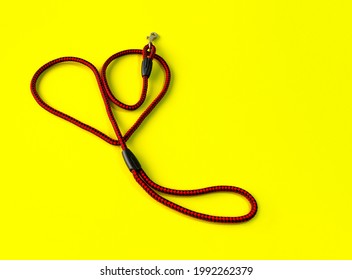 The Dog Leash Is Made Of Round Red And Black Nylon Rope. It Is Arranged In A Cute Heart Shape, Placed On A Yellow Background. Isolated.