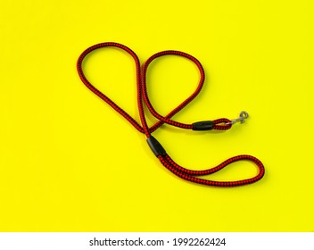 The Dog Leash Is Made Of Round Red And Black Nylon Rope. It Is Arranged In A Cute Heart Shape, Placed On A Yellow Background. Isolated.