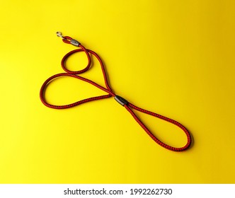 The Dog Leash Is Made Of Round Red And Black Nylon Rope. It Is Arranged In A Cute Heart Shape, Placed On A Yellow Background. Isolated.