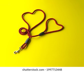 The Dog Leash Is Made Of Round Red And Black Nylon Rope. It Is Arranged In A Cute Heart Shape, Placed On A Yellow Background. Isolated.