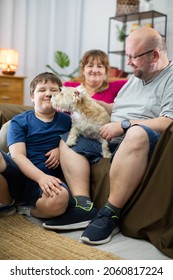 A Dog Licks The Face Of A Boy Who Is Sitting On The Living Room Sofa With His Parents.