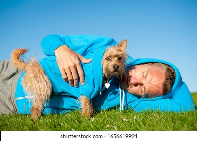 Dog Owner With Best Friend In Matching Blue Hoody Sweatshirts Resting Outdoors On Sunny Green Field