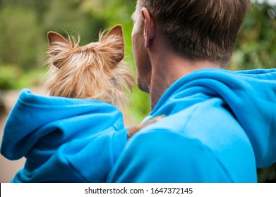 Dog And Owner In Matching Blue Hoodies Standing Outdoors In Bright Green Park Background