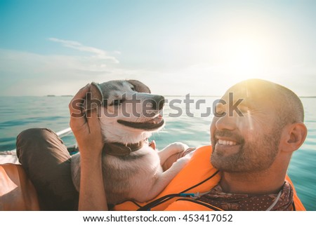 Dog and owner on yacht board on the sunset. Friendship concept. Orange yacht and life-jacket. Funny smiling dog.