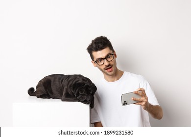 Dog Owner Taking Selfie With Cute Lying Pug, Making Photos On Mobile Phone, White Background