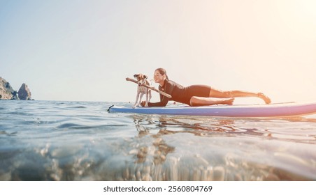 Dog Paddleboarding Woman Ocean - Woman and dog paddleboarding on a sunny day with clear blue water and rocky cliffs in the background. - Powered by Shutterstock