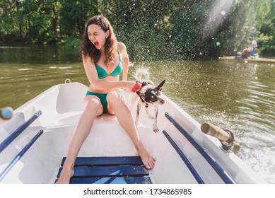 Dog shakes off water sitting on a boat with a girl.