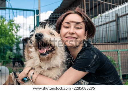 Dog at the shelter. Animal shelter volunteer feeding the dogs. Lonely dogs in cage with cheerful woman volunteer