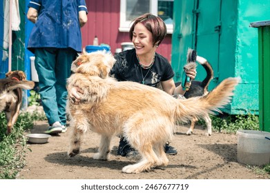 Dog at the shelter. Animal shelter volunteer takes care of dogs. Lonely dogs in cage with cheerful woman volunteer.  - Powered by Shutterstock