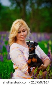 Dog and women concept - A young plump blonde woman hugs and kisses her beautiful black dog in a pink and purple flower field.