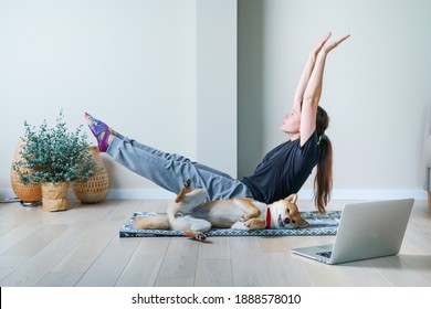 Doga Or Doga Yoga Is The Practice Of Yoga As Exercise With Dogs. Young Woman In Yoga Position Balancing With Her Dog. Home Online Training With A Pet