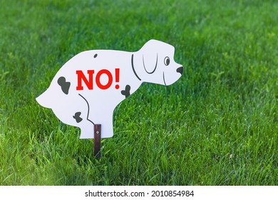 Dogs Are Not Allowed To Poop. A Sign In The Form Of A Dog That Sat Down To Go To The Toilet With The Inscription No. On The Background Of A Bright Green Grass.