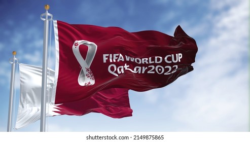Doha, Qatar, January 2022: Flags Qatar 2022 World Cup logo waving among Qatar national flag in the wind. The event is scheduled in Qatar from 21 November to 18 December 2022