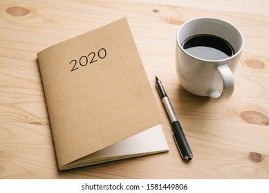 Doing 2020 Newyear Plan With Notebook And Pen. 2020 Schedule Book And A Cup Of Coffee Placing On A Wooden Table.