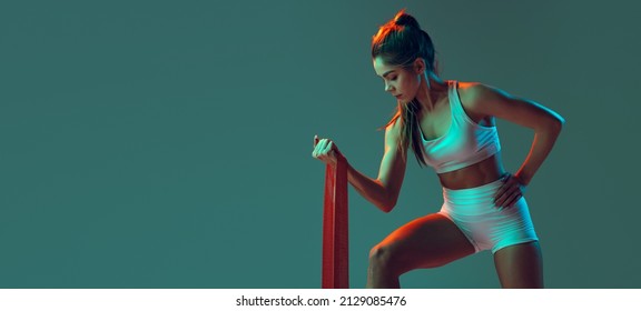 Doing dumb  bell curls  Portrait sportive woman workout  doing exercises and sports equipment isolated green studio background in neon light  Sport  gym  action  motion  beauty concept 