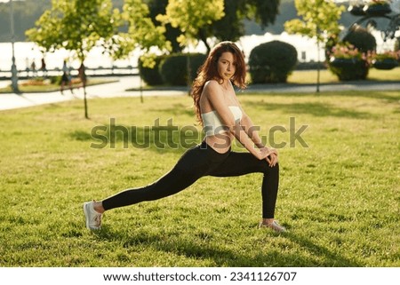 Doing fitness. Beautiful young woman in sportive clothes is in the park at sunny daytime.