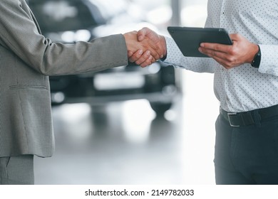 Doing handshake. Man in formal wear helping customer with choice of the automobile. Foto Stock