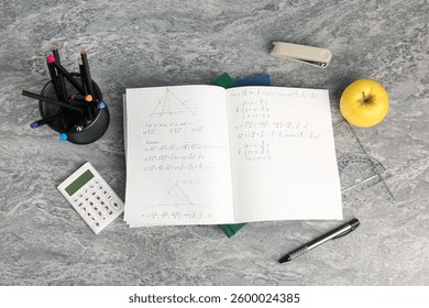 Doing homework. Notebook with math assignment, apple and stationery on grey desk, flat lay