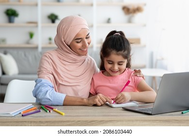 Doing Homework Together. Loving Muslim Mom Helping Her Little Daughter With Study While Sitting Together At Desk With Laptop Computer, Cute Preteen Girl Writing In Notepad And Smiling, Closeup - Powered by Shutterstock