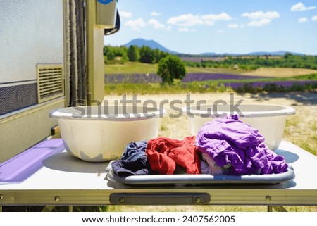 Doing laundry on vacation trip. Bowls with clothes at caravan vehicle. Camping on nature.