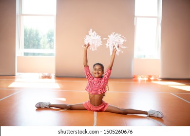 Doing leg split. Dark-skinned little cheerleader smiling while doing leg split while practicing