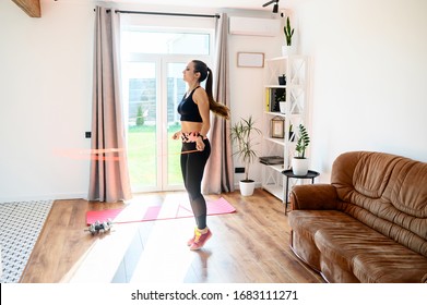 Doing Sports At Home During Quarantine. A Young Woman Jumps With A Skipping Rope Indoors. Cardio Workout At Home