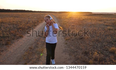 doing sports jogging at sunset outside city. young girl in white T-shirt trains at sunset and listens to music with headphones.