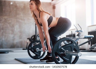 Doing squating with black barbell. Photo of gorgeous blonde woman in the gym at her weekend time. - Shutterstock ID 1410507578