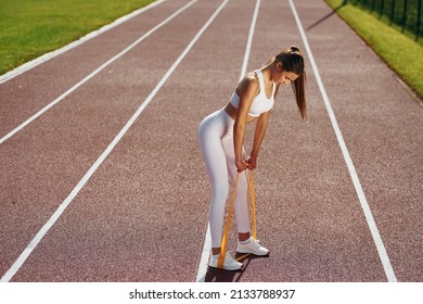 Doing stretching by using tape. Young woman in sportive clothes is exercising outdoors.