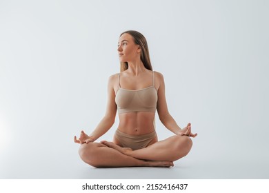 Doing yoga exercises. Woman in underwear with slim body type is posing in the studio.