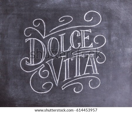 Dolce vita hand drawn lettering on black chalkboard background, italian phrase Sweet life. Vintage design.