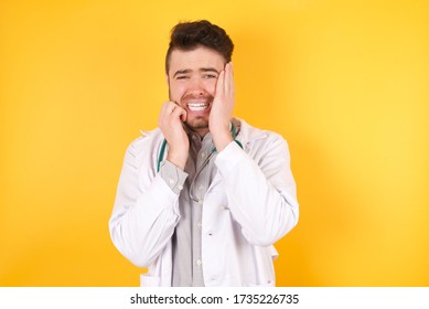 Doleful Desperate Crying Doctor Man Wearing Medical Uniform, Being In Depression After Quarrel With Someone, Looks Stressfully, Frowns Face, Isolated Yellow Wall . Pretty Male Feels Lonely And Anxious