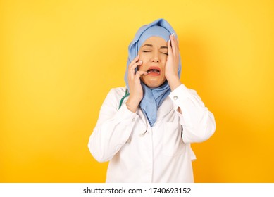 Doleful Desperate Crying Muslim Doctor Woman Wearing Medical Uniform, Being In Depression After Quarrel With Someone, Looks Stressfully, Frowns Face, Isolated Over Yellow Background. 