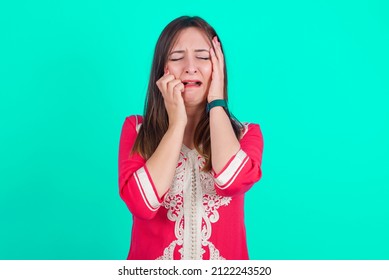 Doleful Desperate Crying Young Beautiful Moroccan Woman Wearing Traditional Caftan Dress Over Green Background, Looks Stressfully, Frowns Face, Feels Lonely And Anxious