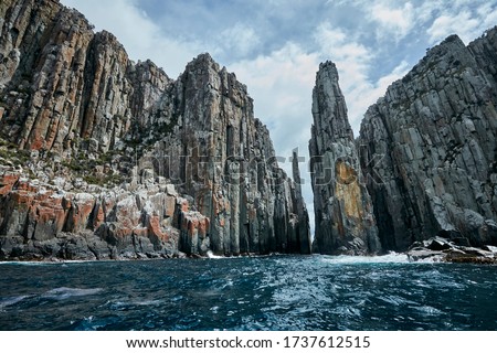 Dolerite cliffs of the Tasman Peninsula as viewed from a boat out at sea.  In the middle are the totem pole and needle, a destination for experienced climbers. Port Arthur, Tasmania, Australia