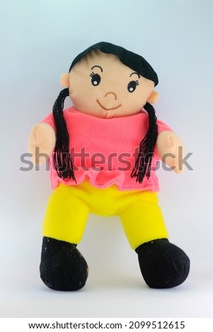 a Doll, in the form of a girl standing with long hair ponytail, wearing a pink shirt, yellow pants, and black shoes.